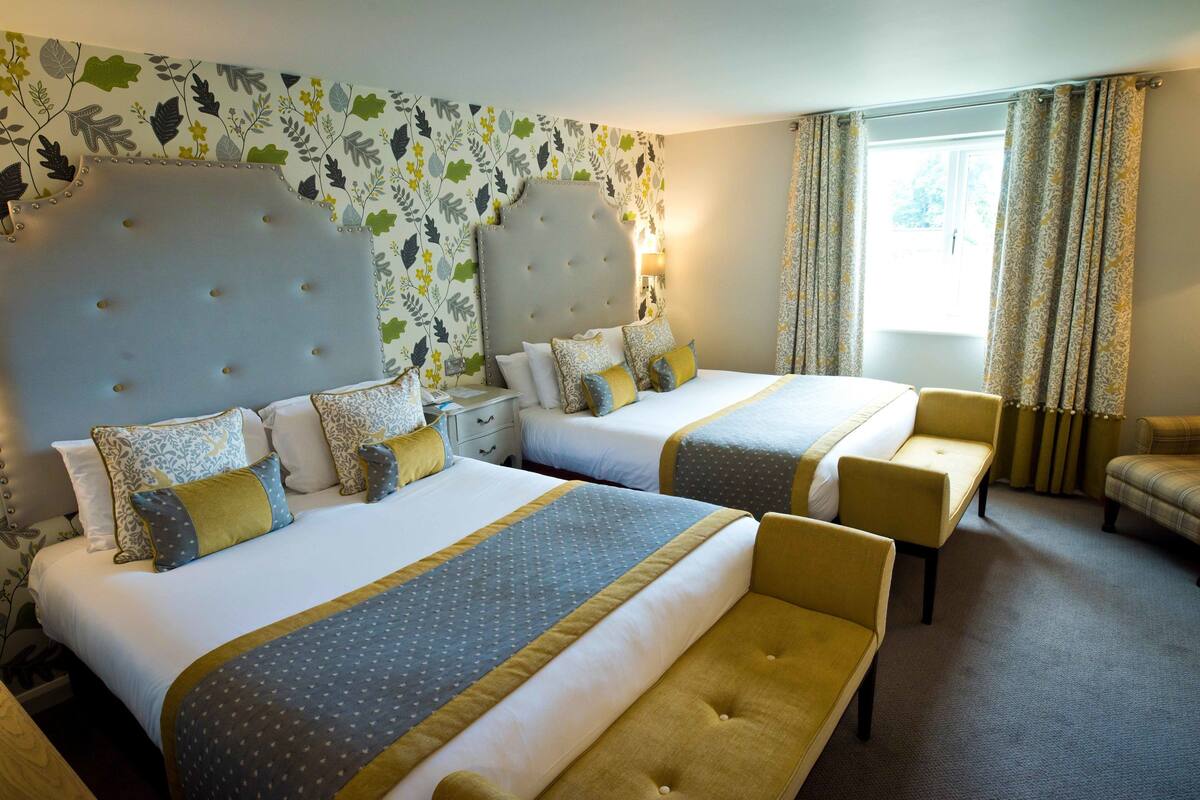 A hotel room with two beds, a sofa, and a window with curtains.