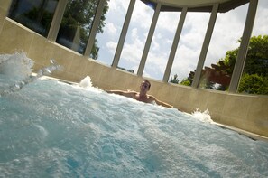 Eine Person in einer Hot-Whirlpool mit Blick auf Bäume und einen klaren Himmel.