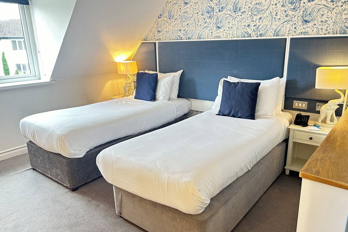 A hotel room with two single beds, a nightstand with a lamp, a telephone, and a decorative cat statue.