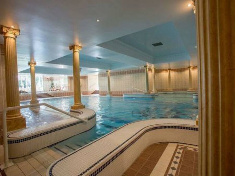 An indoor swimming pool with columns, a hot tub, and a tiled floor.
