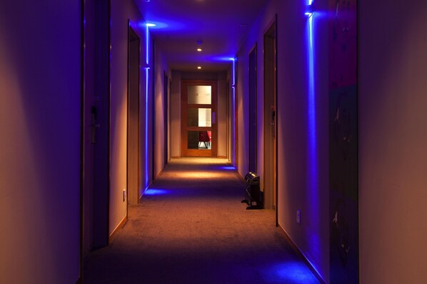 A hotel corridor with a carpeted floor, a door at the end, and blue lighting. - Best Western Atlantic Hotel (Chelmsford)