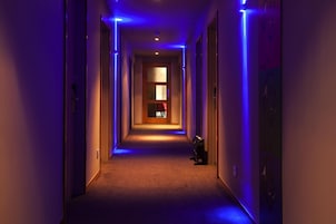 Un pasillo de hotel con suelo alfombrado, una puerta al final y luces azules.