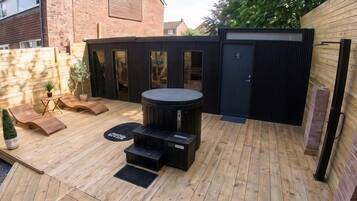 A wooden deck with a hot tub, seating area, and a small table.