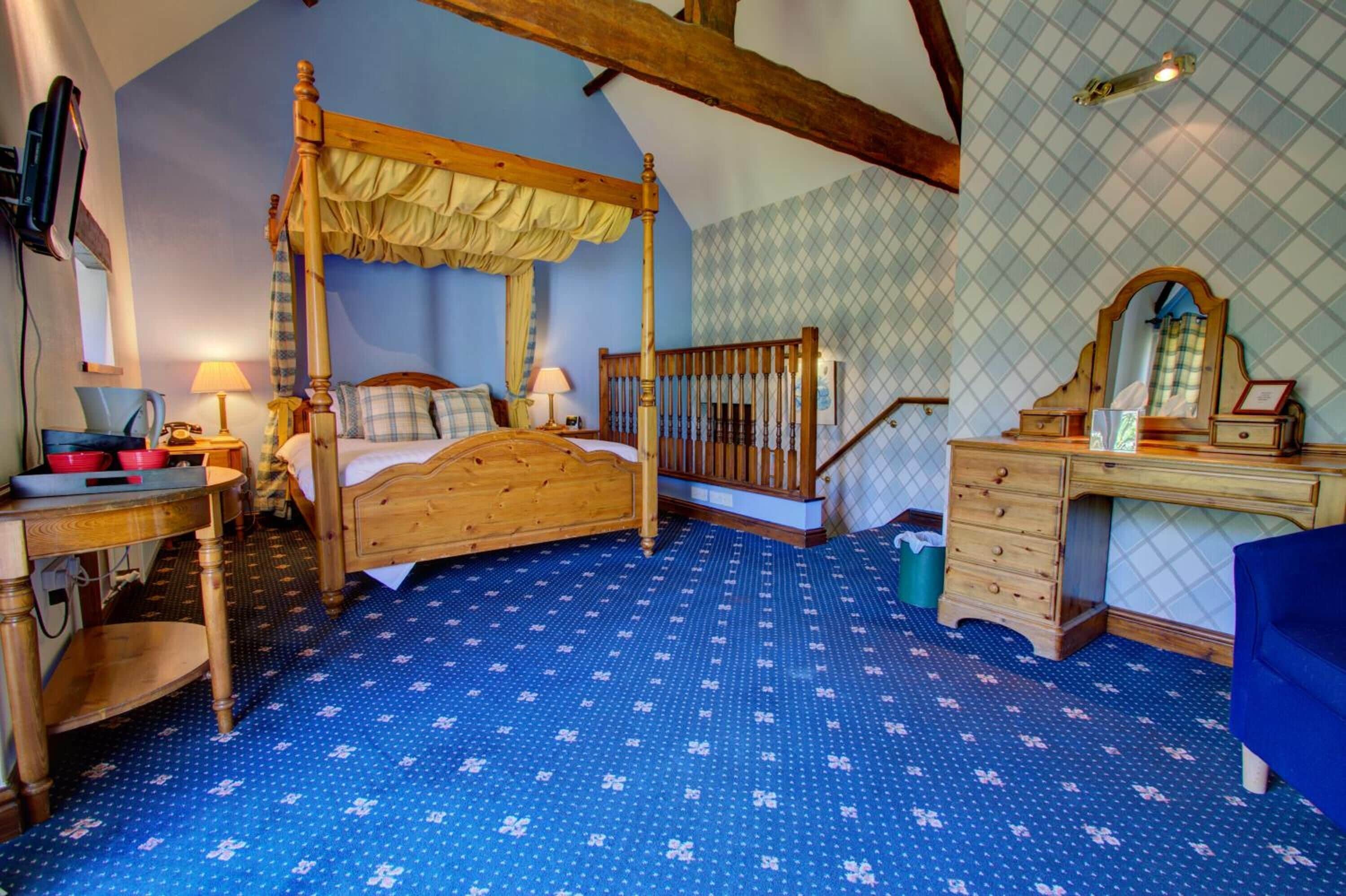 A bedroom with a four-poster bed, wooden desk, and dresser.