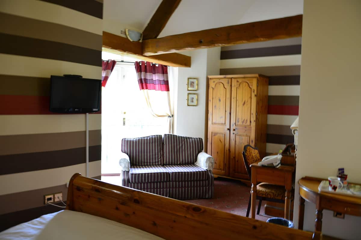 A room with a bed, a striped sofa, a wooden cabinet, and a television on the wall.