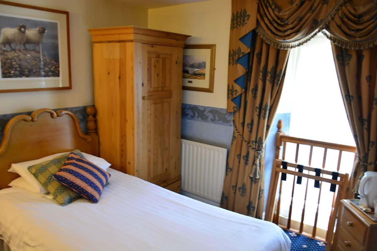 A bed with pillows, a wooden wardrobe, a radiator, and a window with curtains.