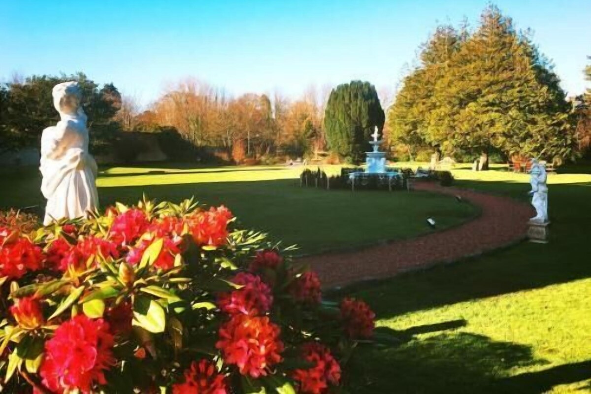 A statue in a garden with a fountain and trees in the background.