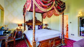Una cama con dosel y cuatro columnas, con elaboradas tallas de madera, un mesita de noche a juego y una alfombra roja con estampado.