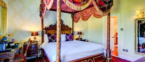 A four-poster canopy bed with ornate wooden carvings, a matching nightstand, and a red patterned carpet.