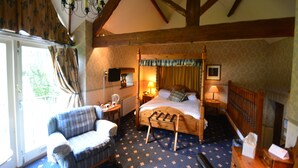 Een traditionele slaapkamer met een hemelbed, een houten bankje, een stoel en een klein tafeltje met een lamp.