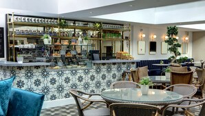 Una zona de bar con barra, estantes con frascos y un área de estar con sillas de mimbre y una mesa redonda.