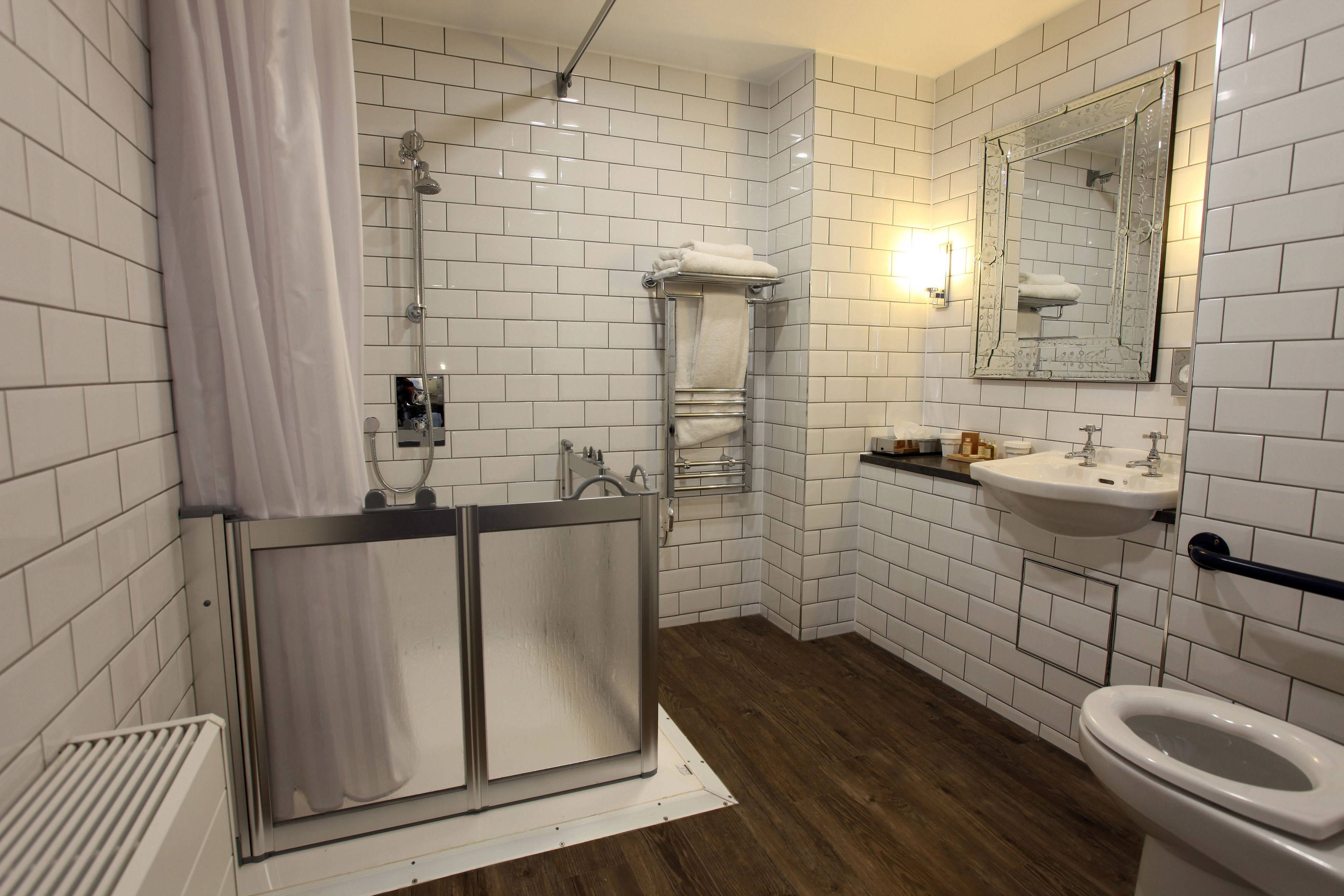 A modern bathroom with white subway tiles, a shower with a glass door, a sink with a mirror, and a toilet.