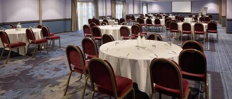 A conference room with multiple round tables, red upholstered chairs, and a large screen at the front.