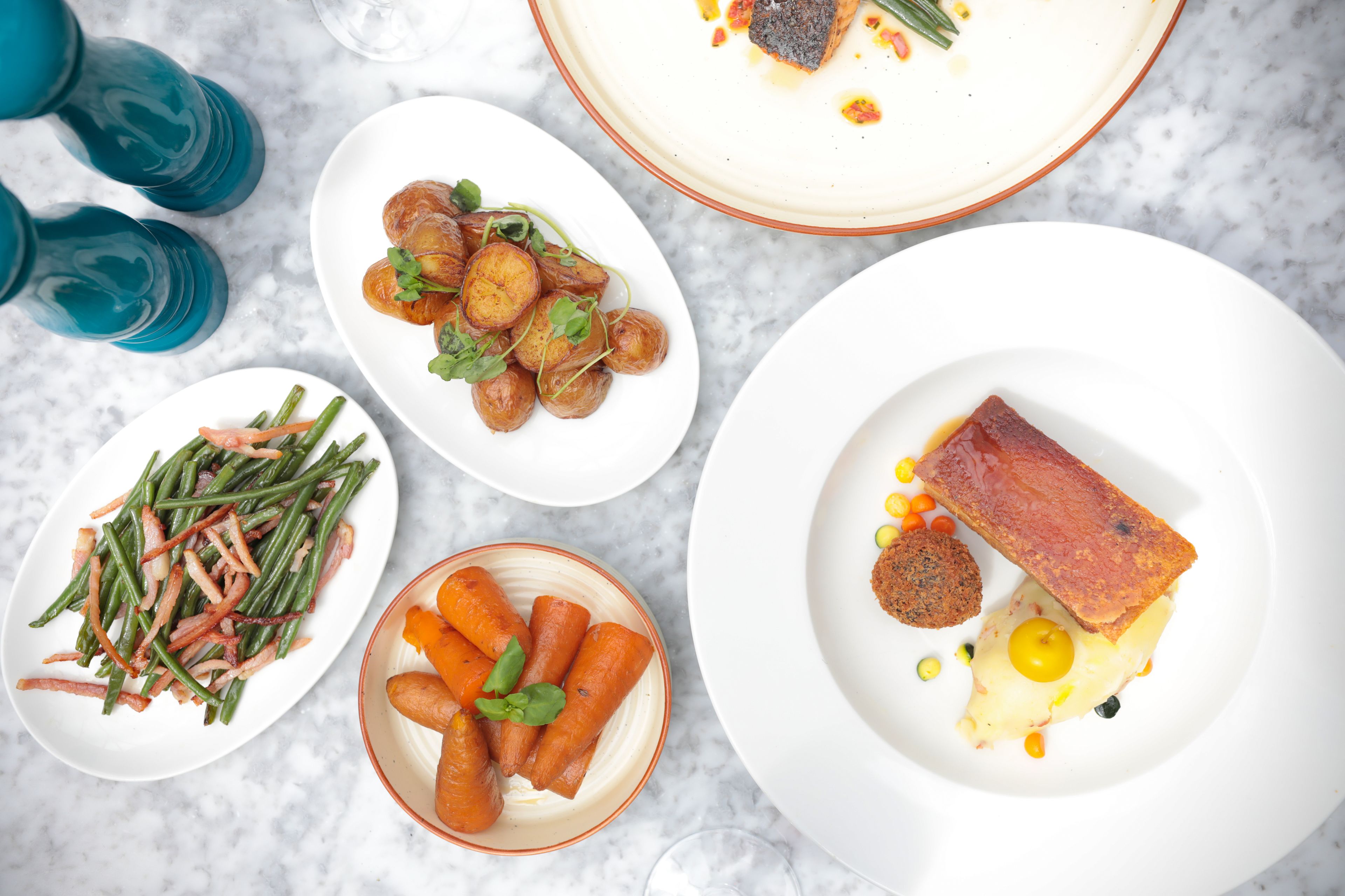 A table with various dishes including roasted potatoes, green beans, carrots, and a piece of meat with corn and a sauce.