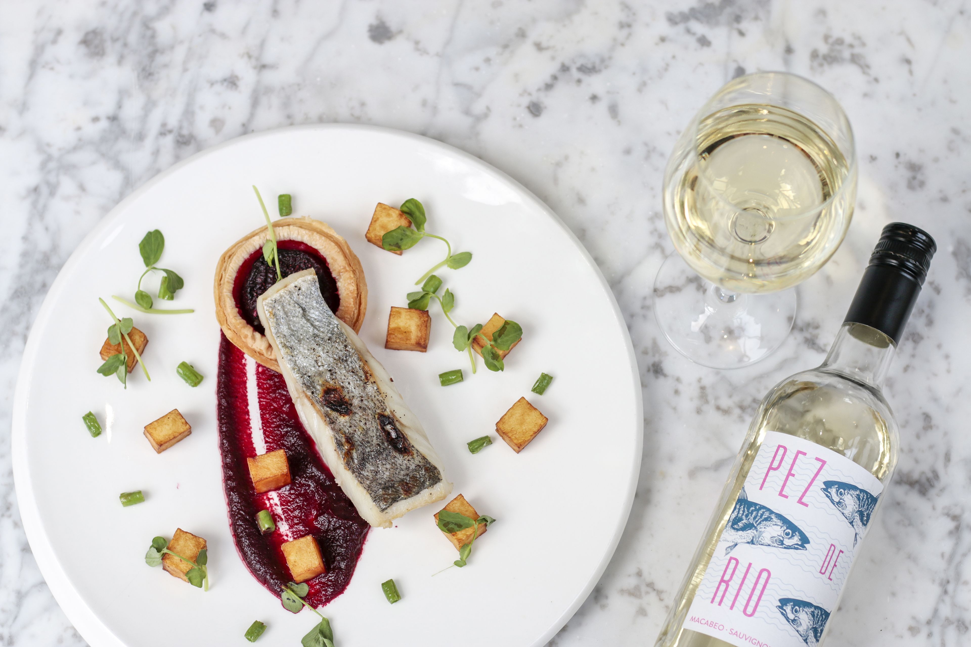 Ein Teller mit Fisch-Tartare, garniert mit grünen Kräutern und Würfeln, und eine Flasche Weißwein mit dem Aufdruck "PEZ DE RIO".
