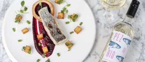 Ein Teller mit Fisch-Tartare, garniert mit grünen Kräutern und Würfeln, und eine Flasche Weißwein mit dem Aufdruck "PEZ DE RIO".