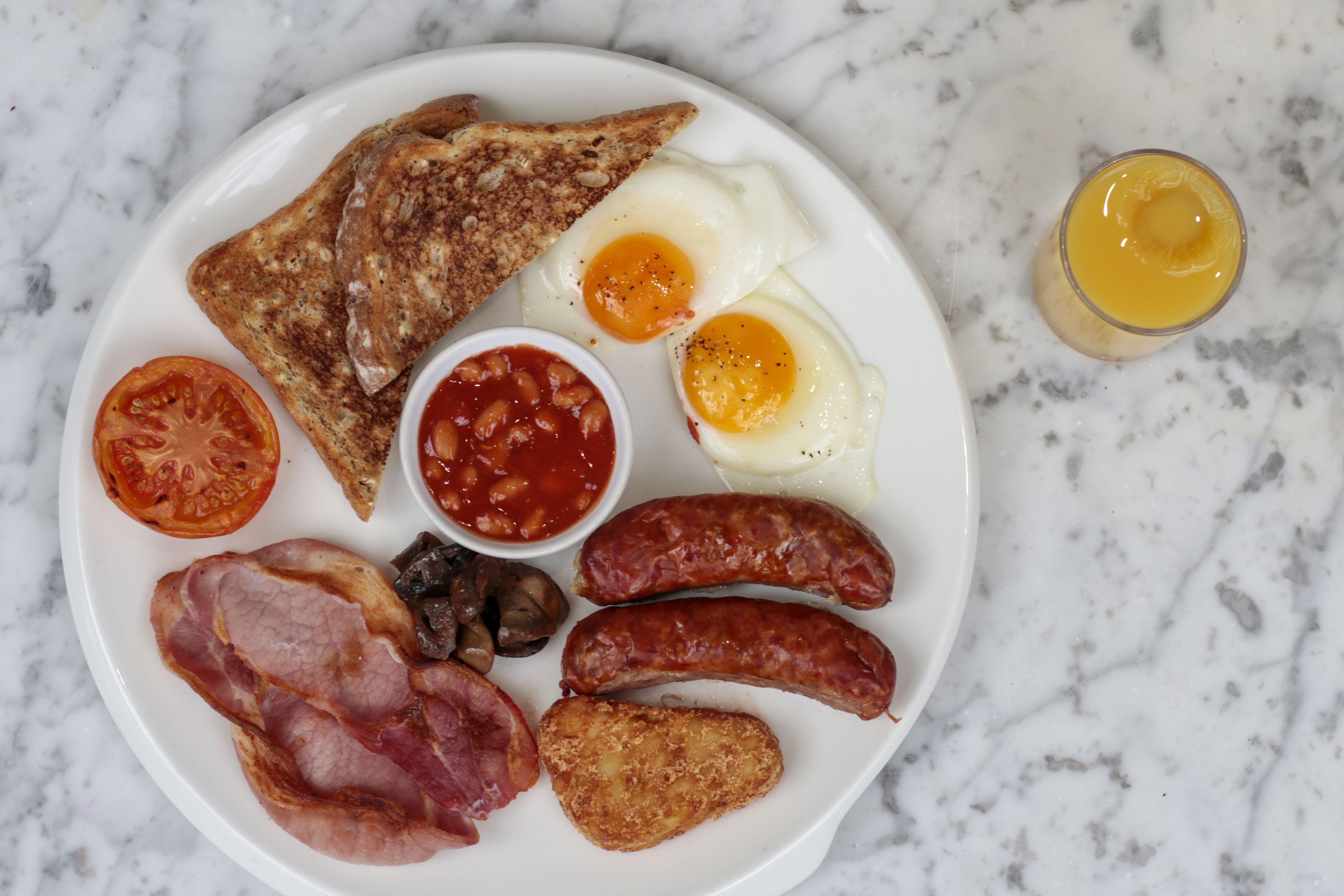 Une assiette de nourriture pour le petit-déjeuner comprenant des toasts, des œufs, des saucisses, des tomates, des haricots et du bacon.