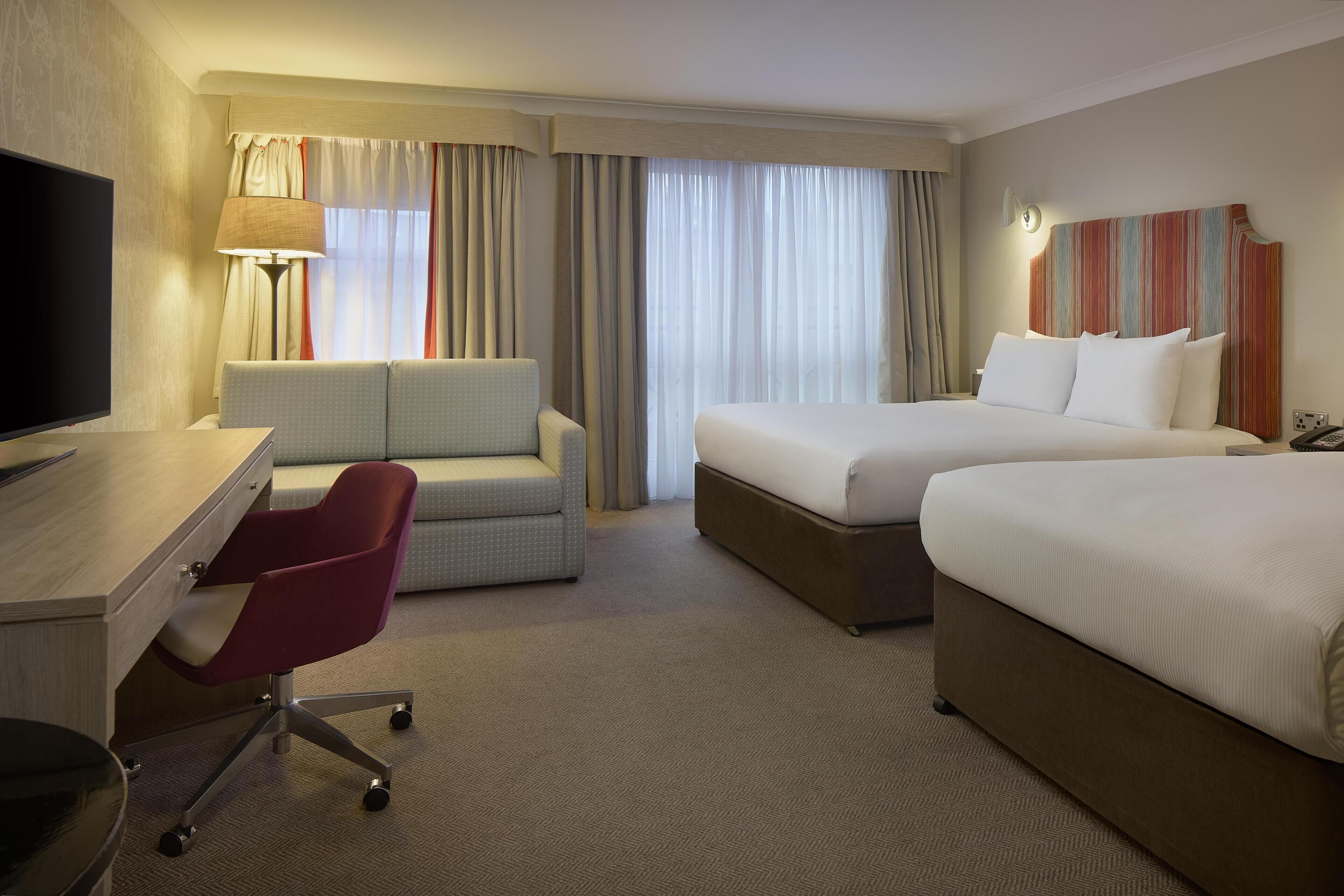 A hotel room with a desk, a red chair, a bed, and a TV.