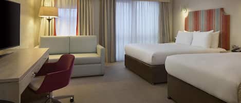 A hotel room with a desk, a red chair, a bed, and a TV.