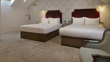 A hotel room with two beds, a skylight, a patterned carpet, and a green upholstered chair.