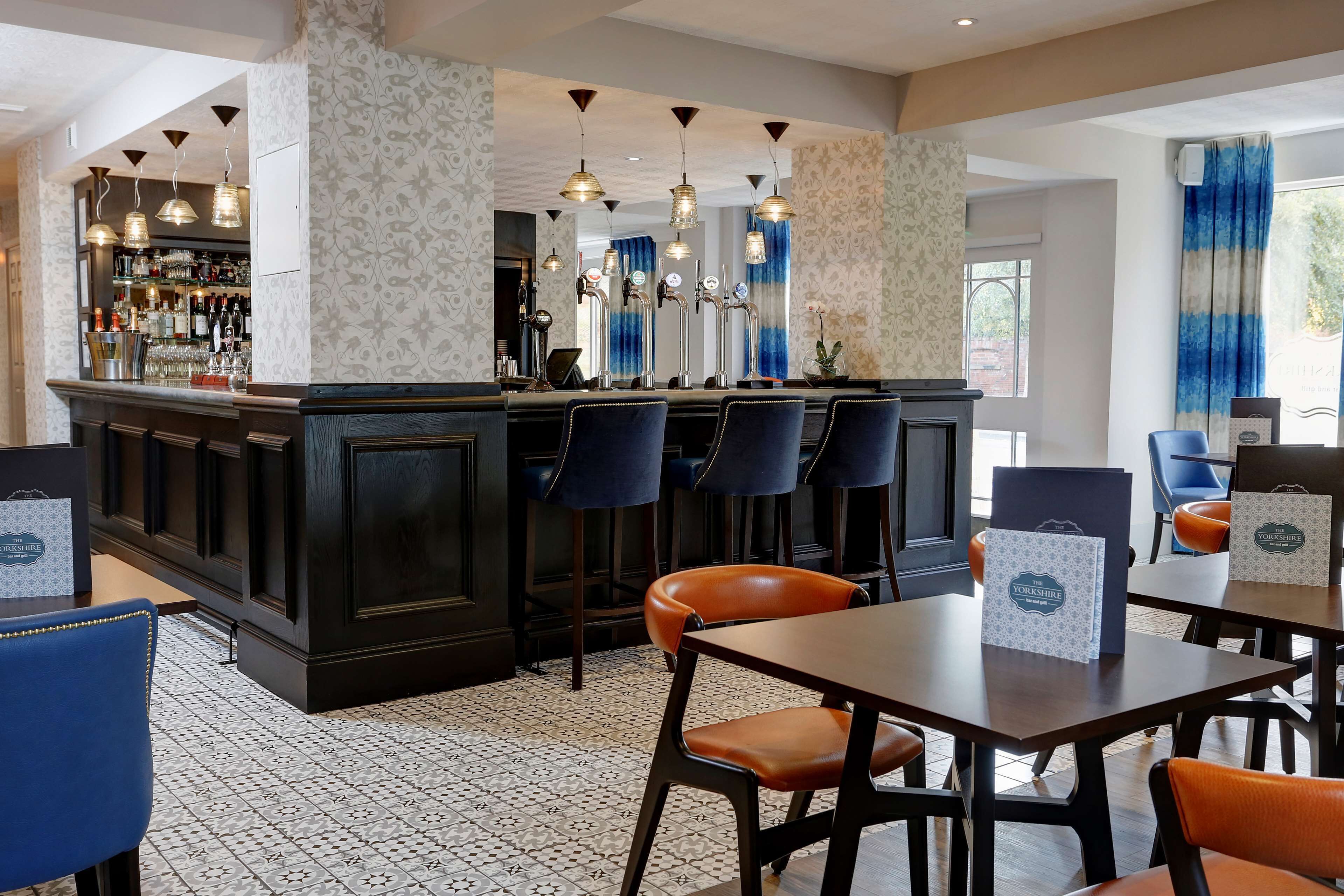 A bar area with a dark counter, multiple bar stools, and a tiled floor.