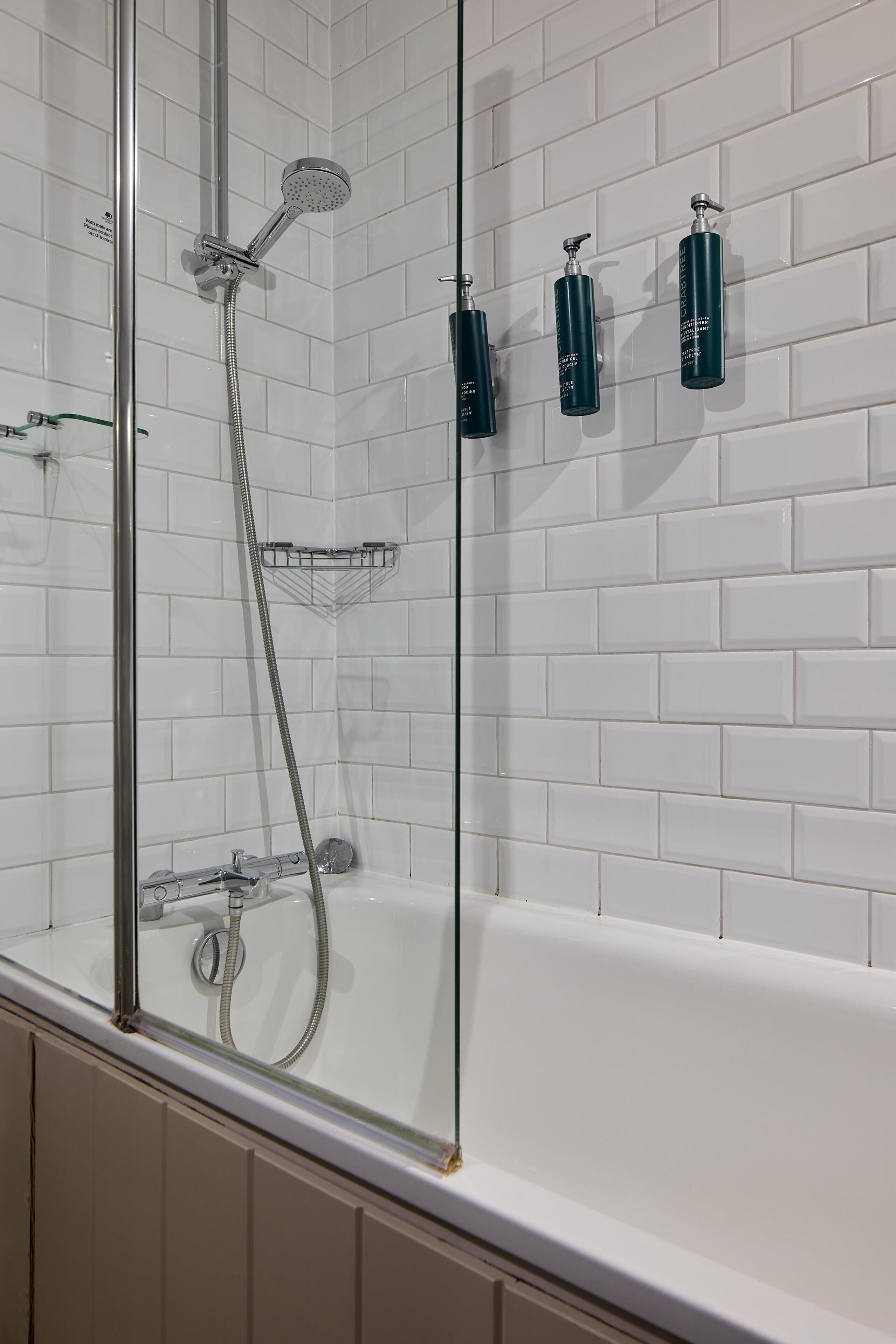 Ein modernes Badezimmer mit einer Glaskabine zur Dusche, einer weißen Badewanne und drei dunkel gefärbten Flaschen an der Wand.