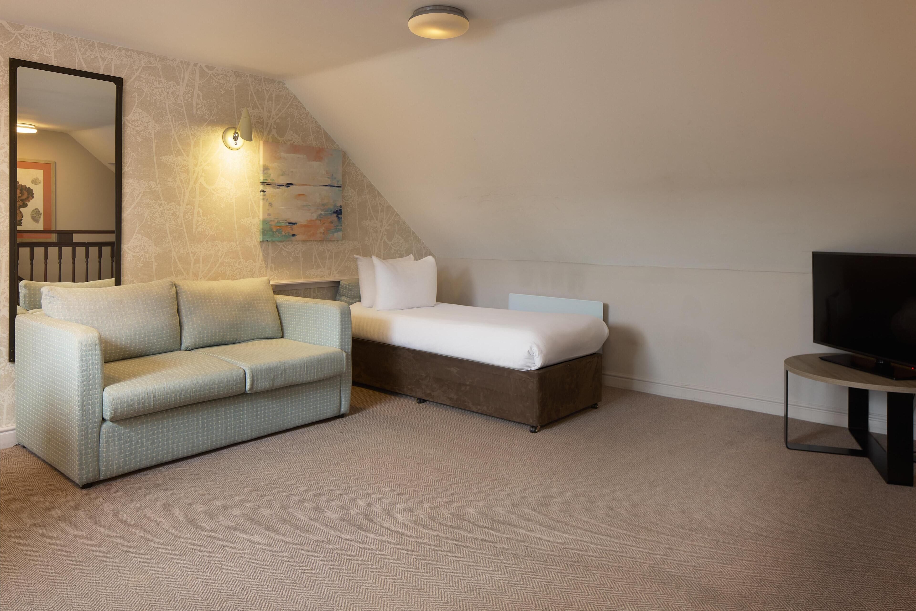 A bedroom with a bed, a sofa, a TV, and a painting on the wall.