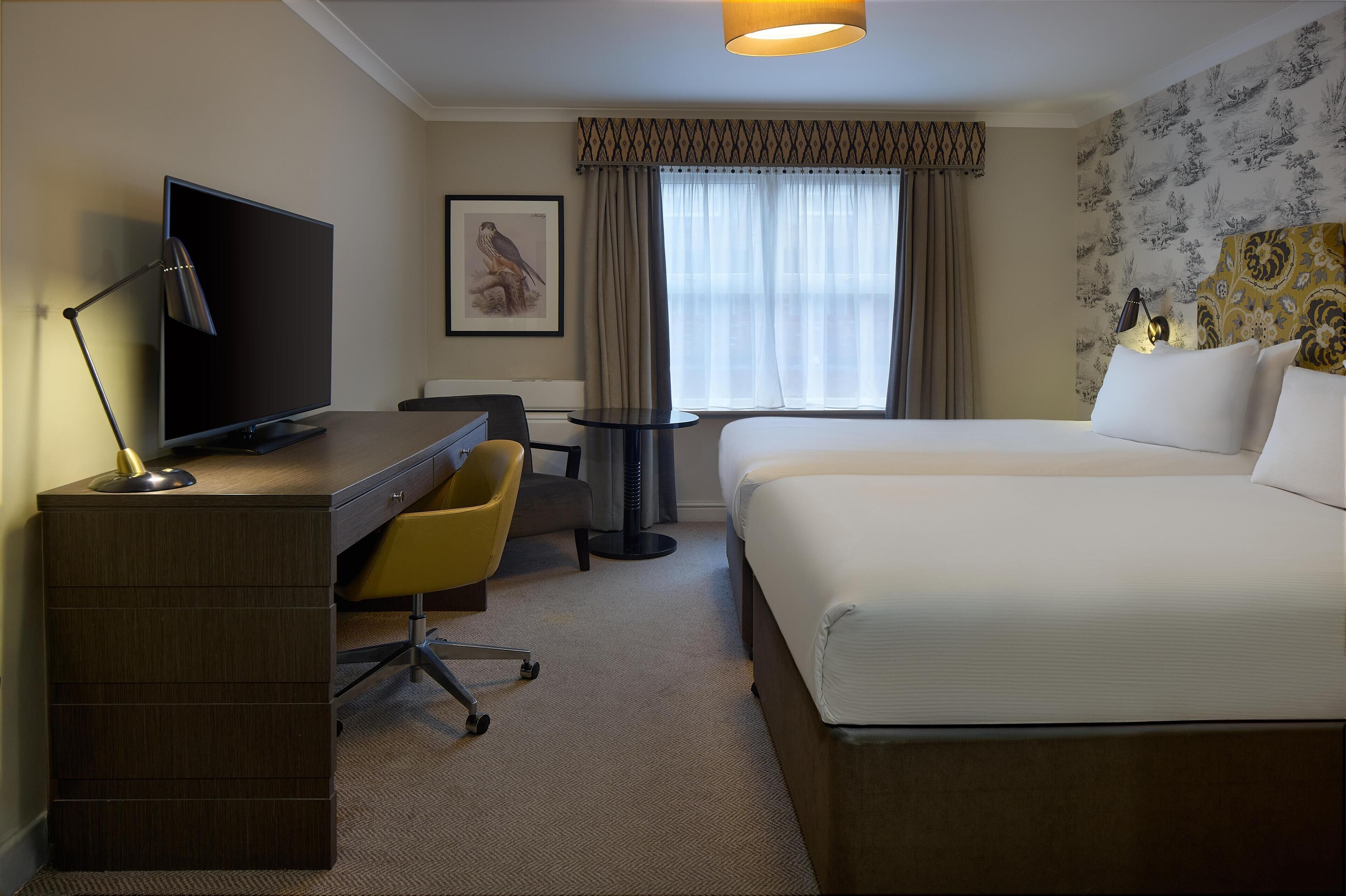 A hotel room with a bed, desk, chair, TV, and a window with curtains.