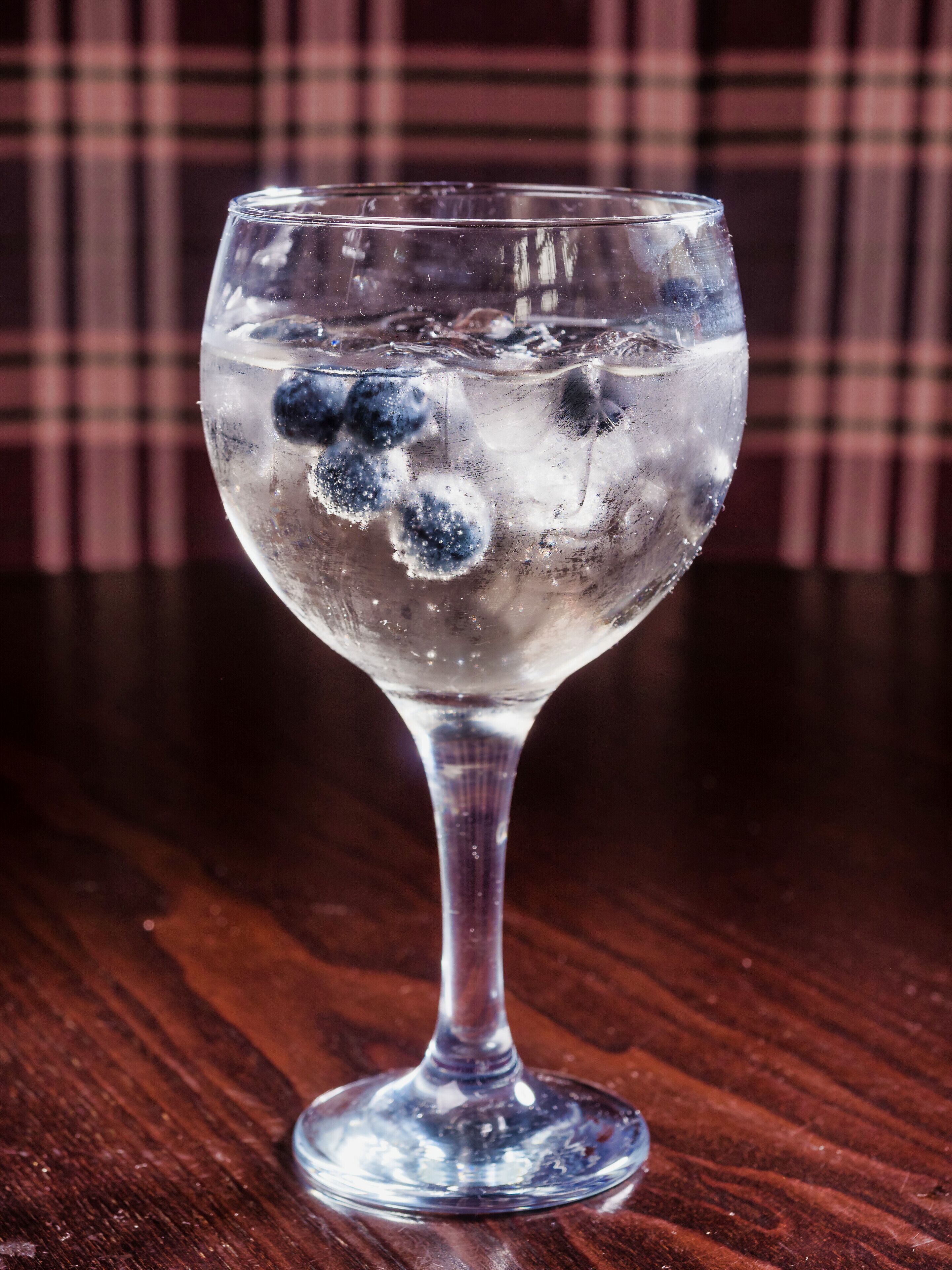 A clear glass with ice and blueberries on a wooden table.