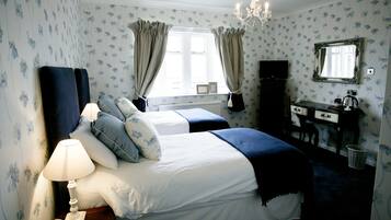 Une chambre avec deux lits, une commode, un miroir, un lustre et une fenêtre avec des rideaux.