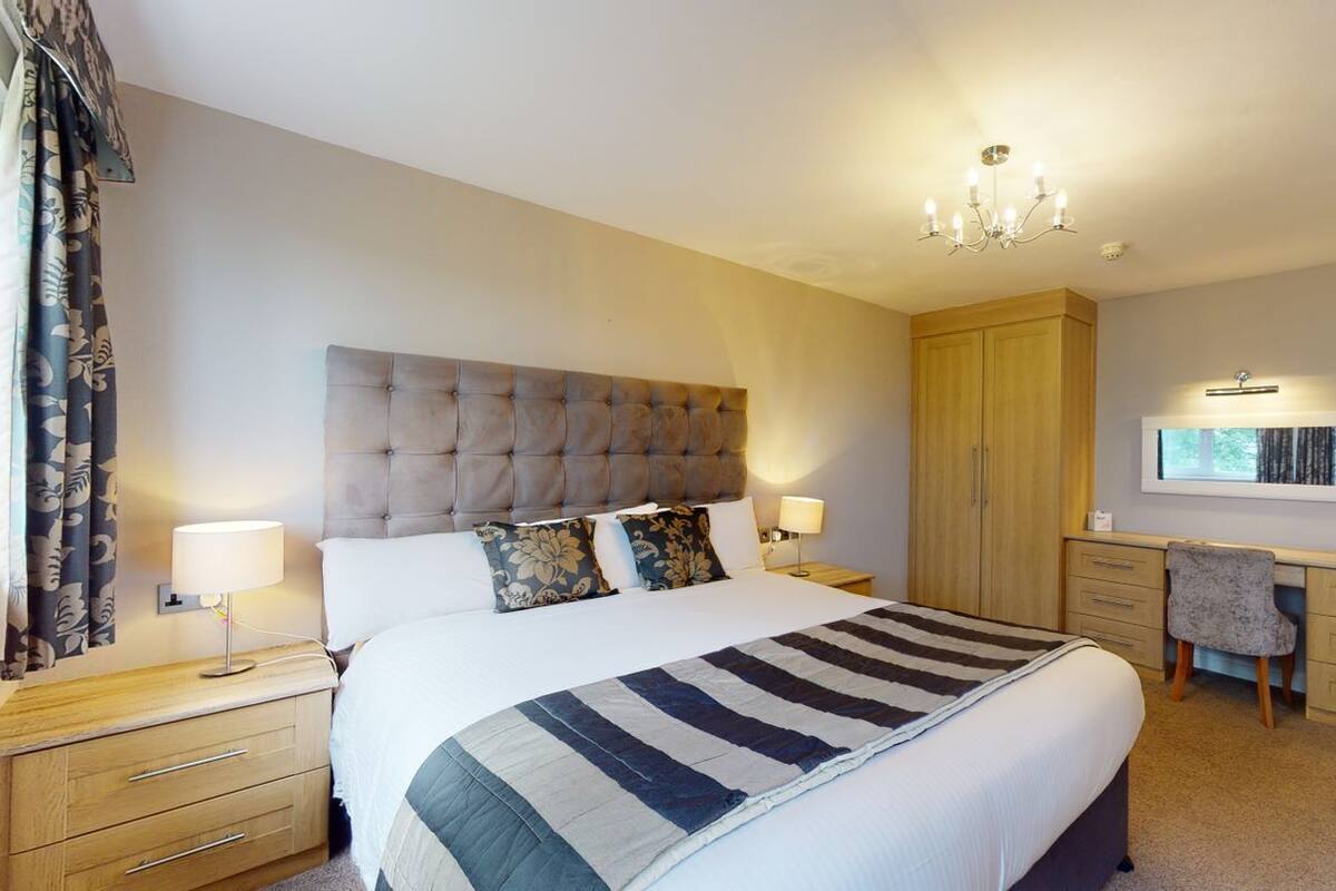 A hotel room with a large bed, a desk, a chair, and a wardrobe.