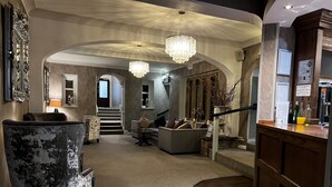 A spacious living area with a grand staircase, a chandelier, and a bar area with bottles.