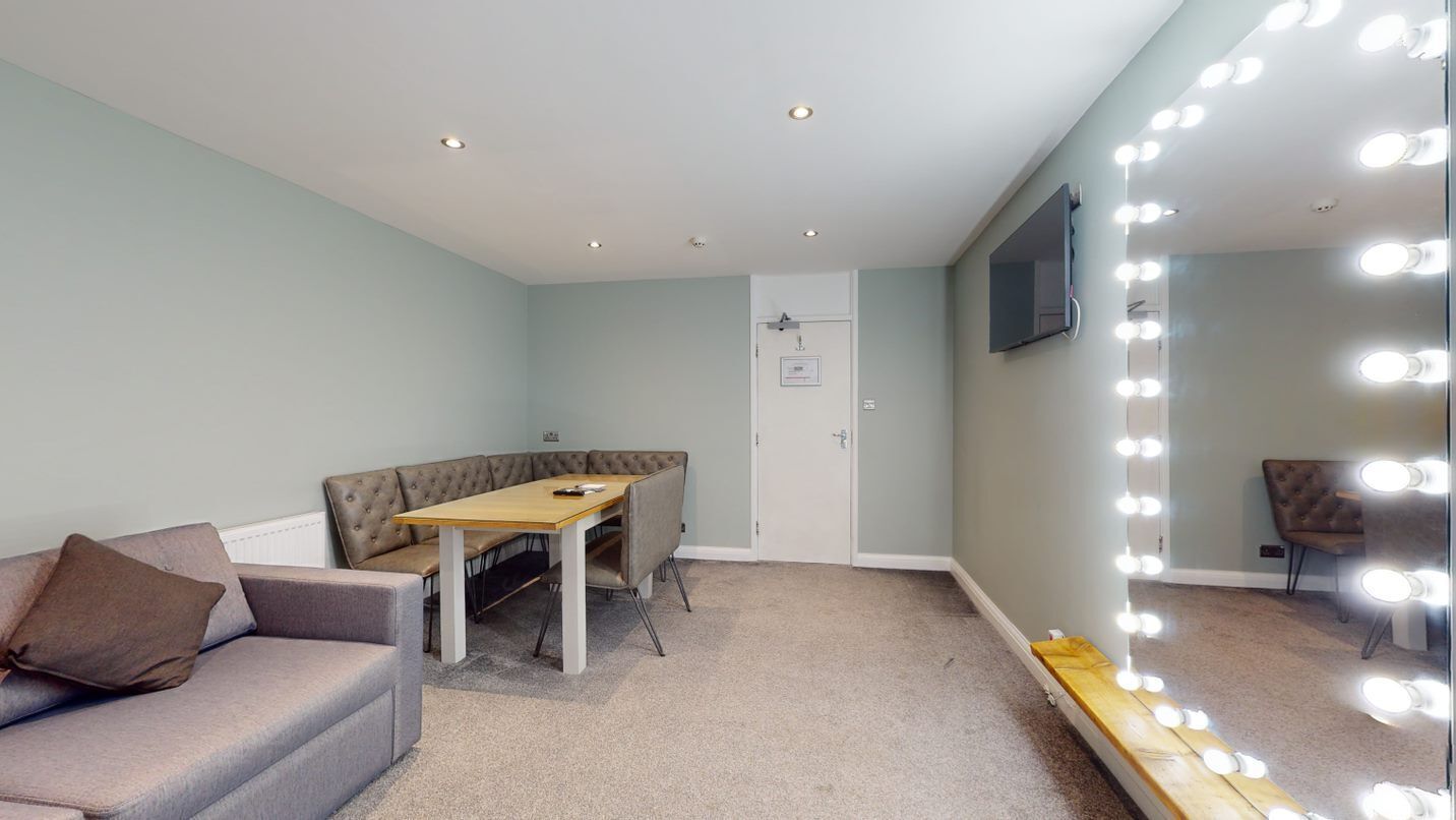 A room with a sofa, a table, and a mirror with lights.