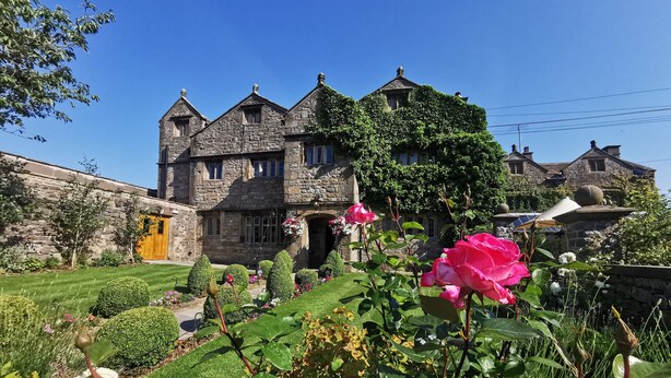 A stone building with a traditional design, featuring multiple chimneys and a well-maintained garden with various plants and flowers.