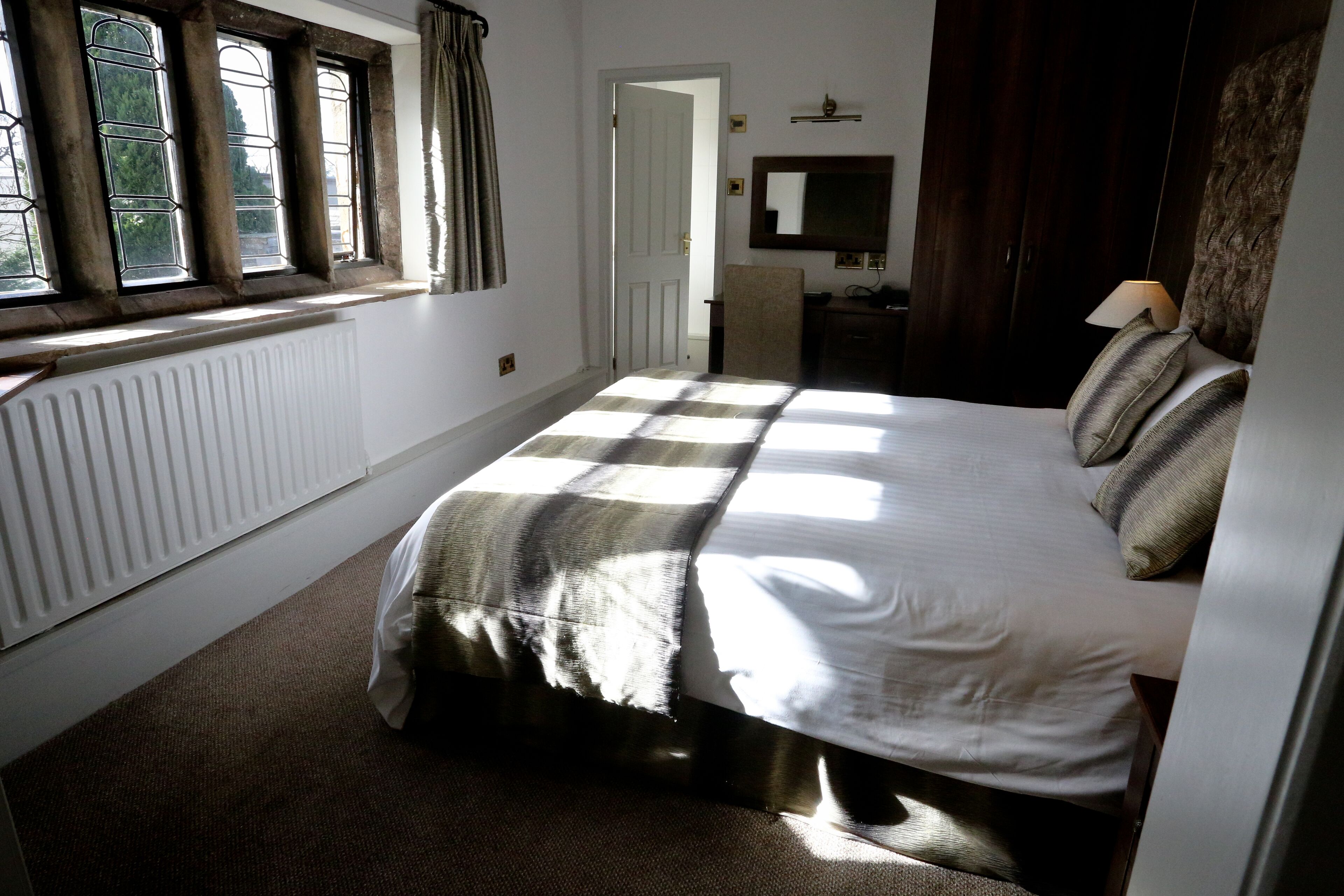 Un dormitorio con una cama grande, un radiador, una ventana con cortinas, un espejo y un aparador.
