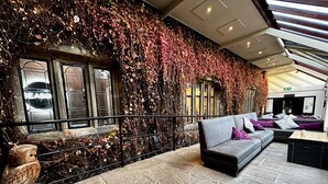 A modern interior with a stone floor, a grey sofa with purple cushions, and a wall covered in vines.