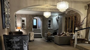 A spacious lobby with a grand staircase, a chandelier, and a mix of seating areas.