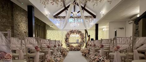 Une allée décorée pour un mariage, agrémentée de compositions florales, de chaises blanches et d’un lustre.