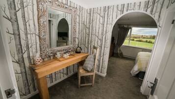A bedroom with a large mirror, a wooden bench, a chair, and a view of the outdoors through an arched window.
