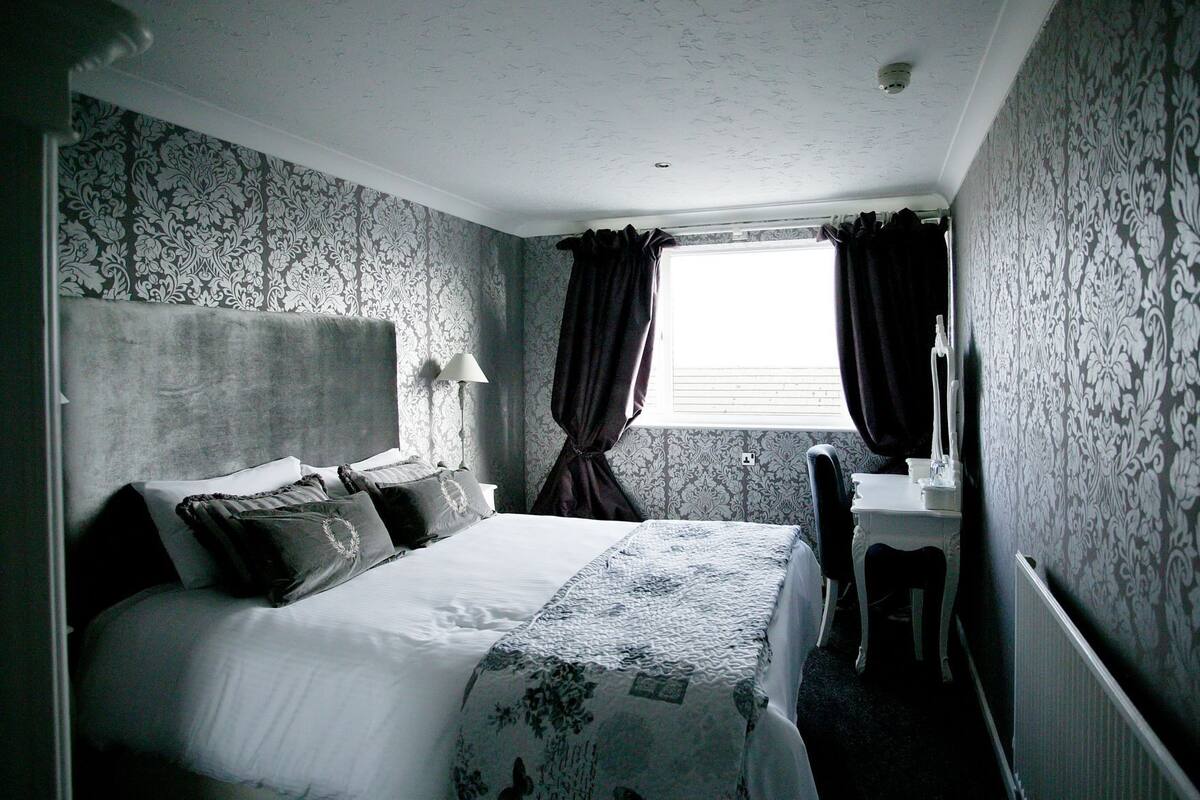 A bedroom with a bed, bedside table, lamp, and a window with curtains.