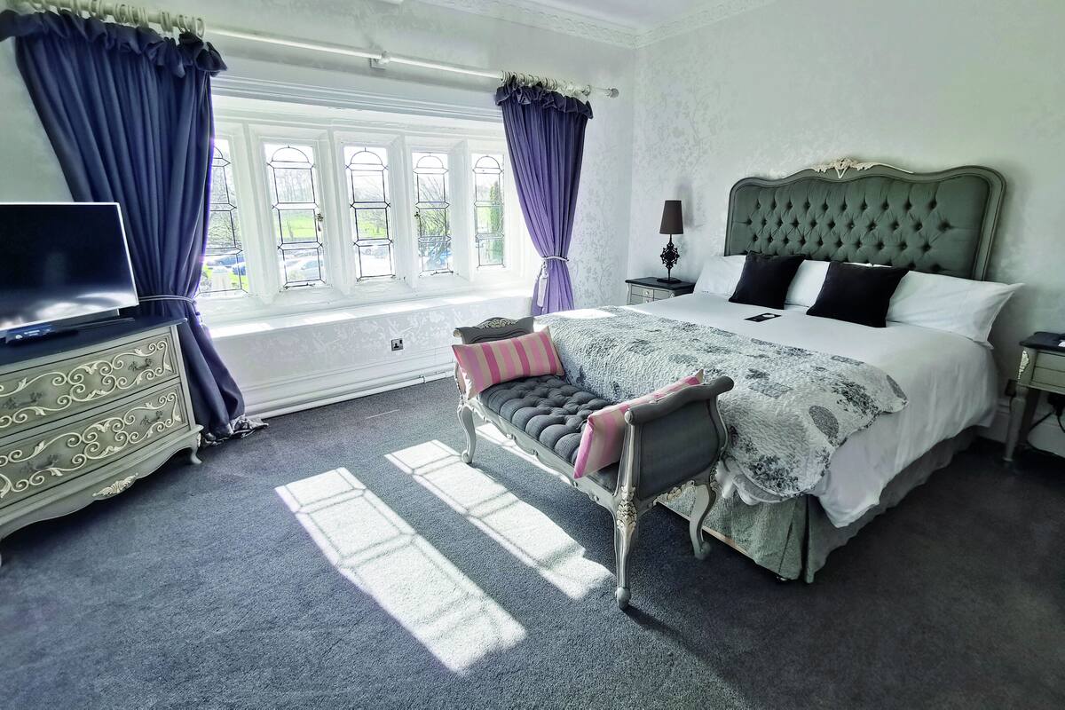 A bedroom with a large bed, a dresser, a TV, and a window with curtains.