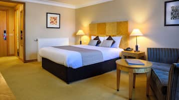 Habitación de hotel con una cama grande, dos lámparas de noche, una mesita, una silla y un cuadro en la pared.