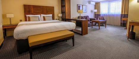 A hotel room with a large bed, a bench, a desk, a chair, and a sofa.