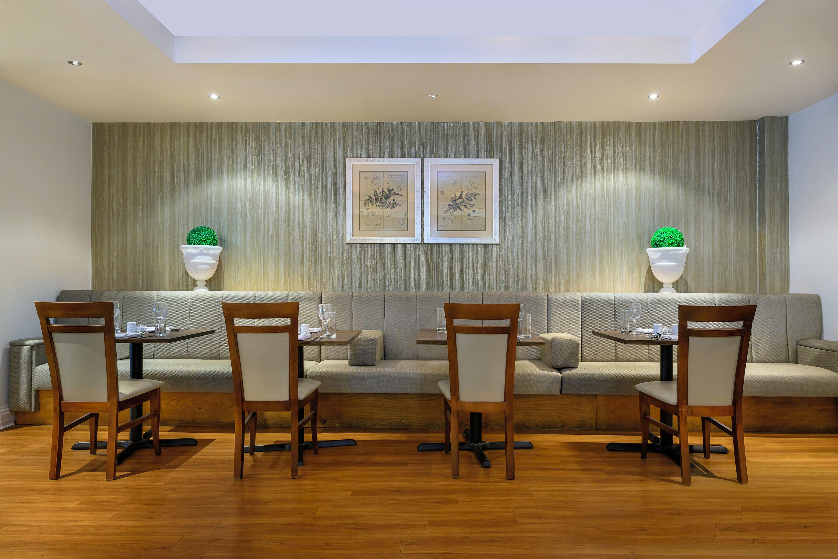 A dining area with a wooden floor, a sofa, and two tables with chairs. There are two wall-mounted planters with green plants.