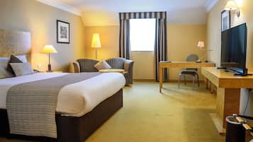Una habitación de hotel con cama, escritorio, silla, televisor y ventana con cortinas.