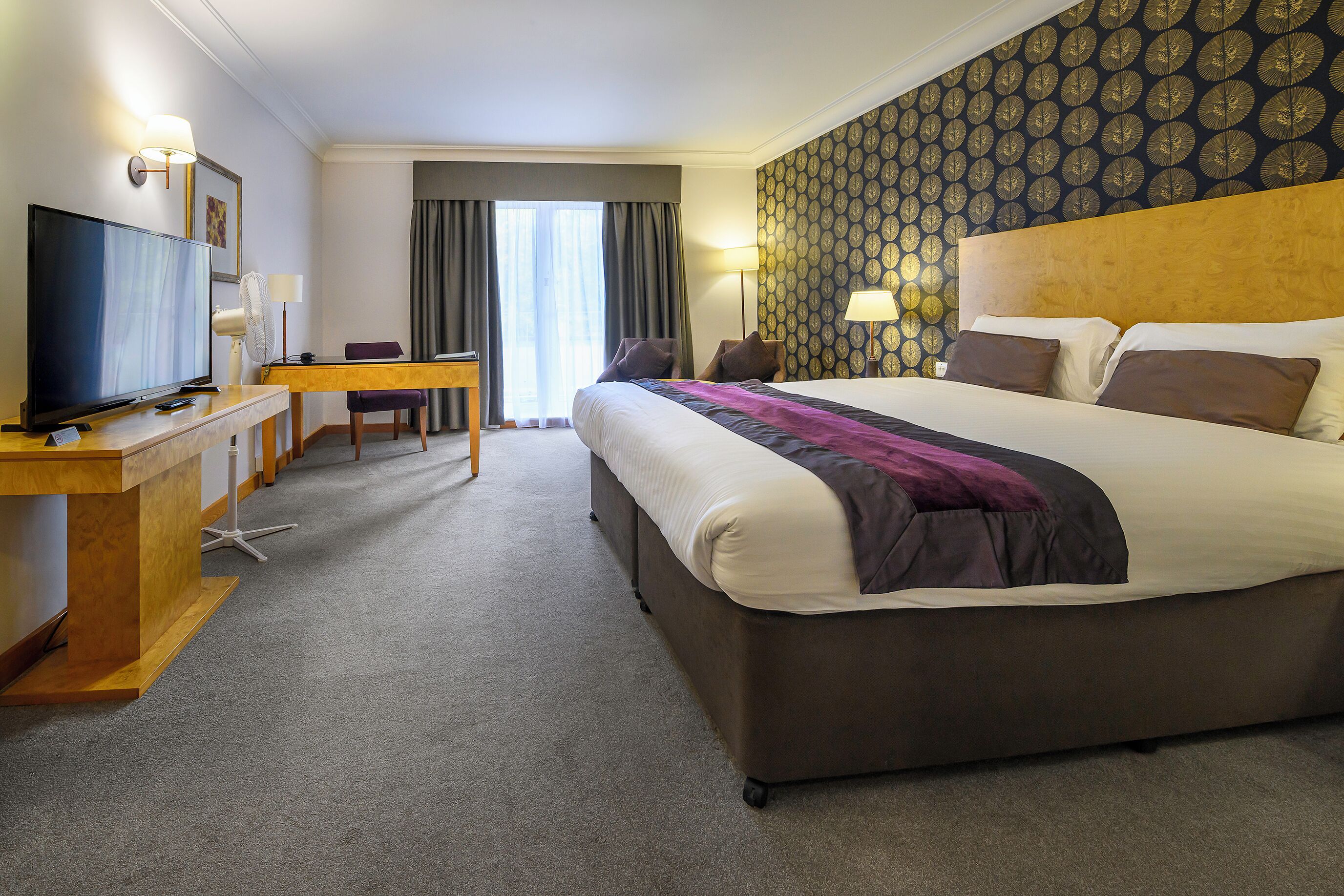 Ein Hotelzimmer mit einem großen Bett, einem Schreibtisch mit Fernseher und Blick ins Freie durch das Fenster.