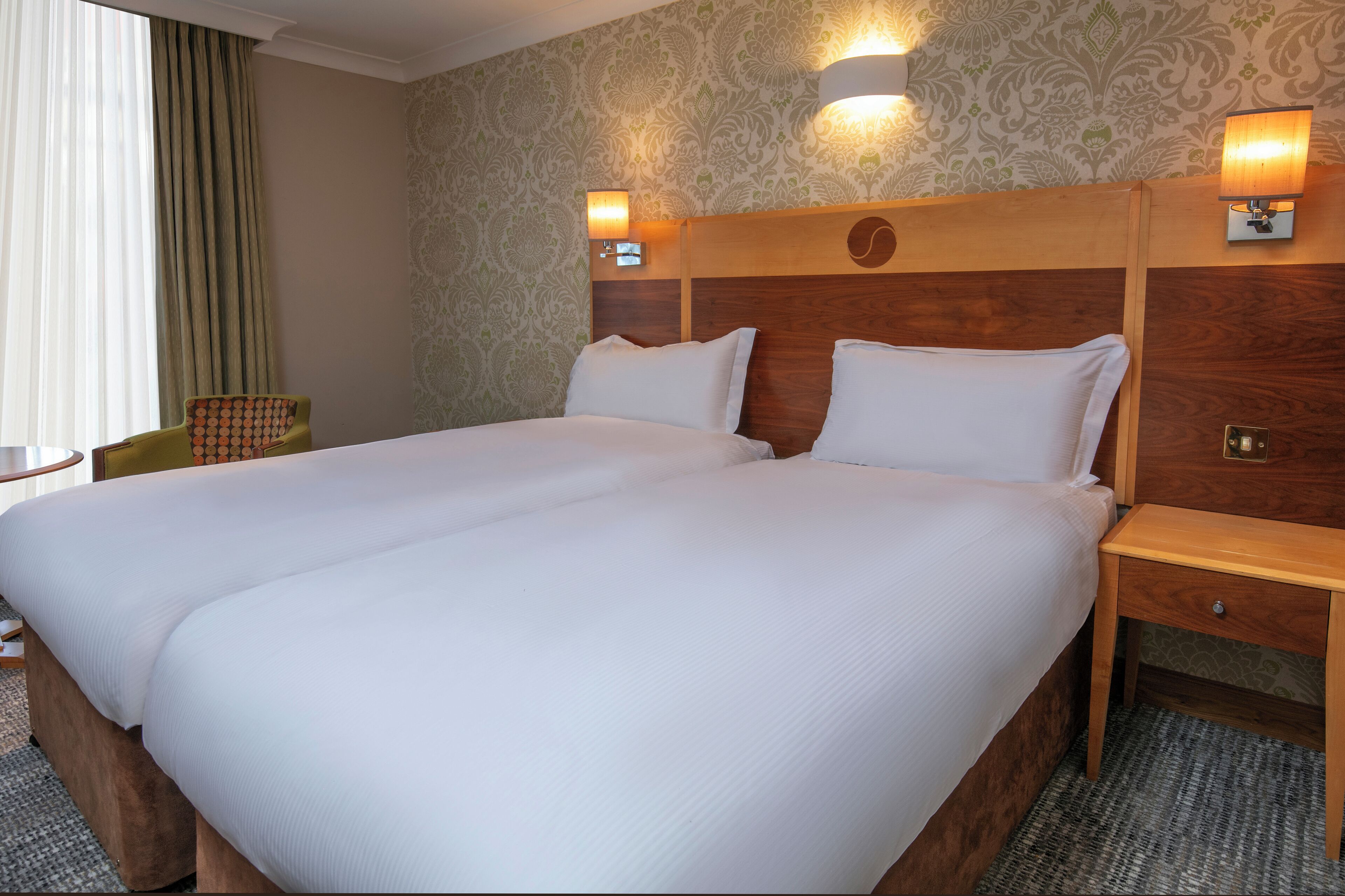 A double bed with two pillows, a wooden headboard, bedside tables, and a chair.