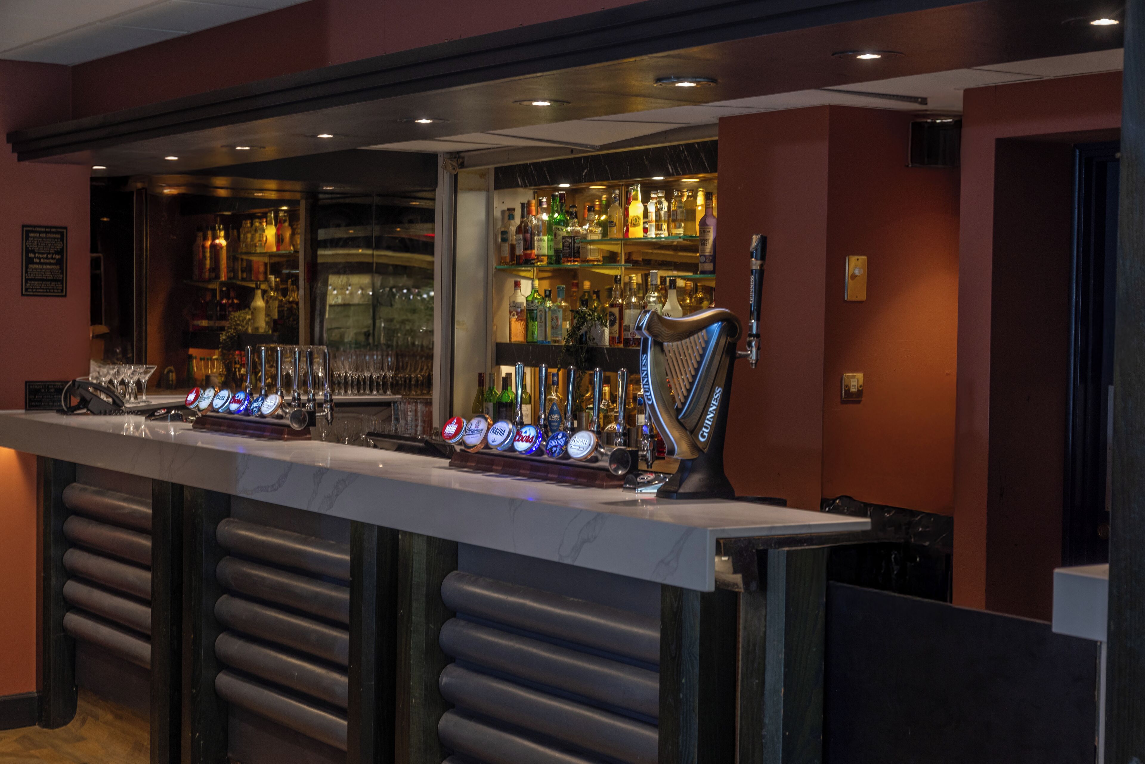 Zona de bar con una barra larga, varias llaves dispensadoras y estantes llenos de botellas.