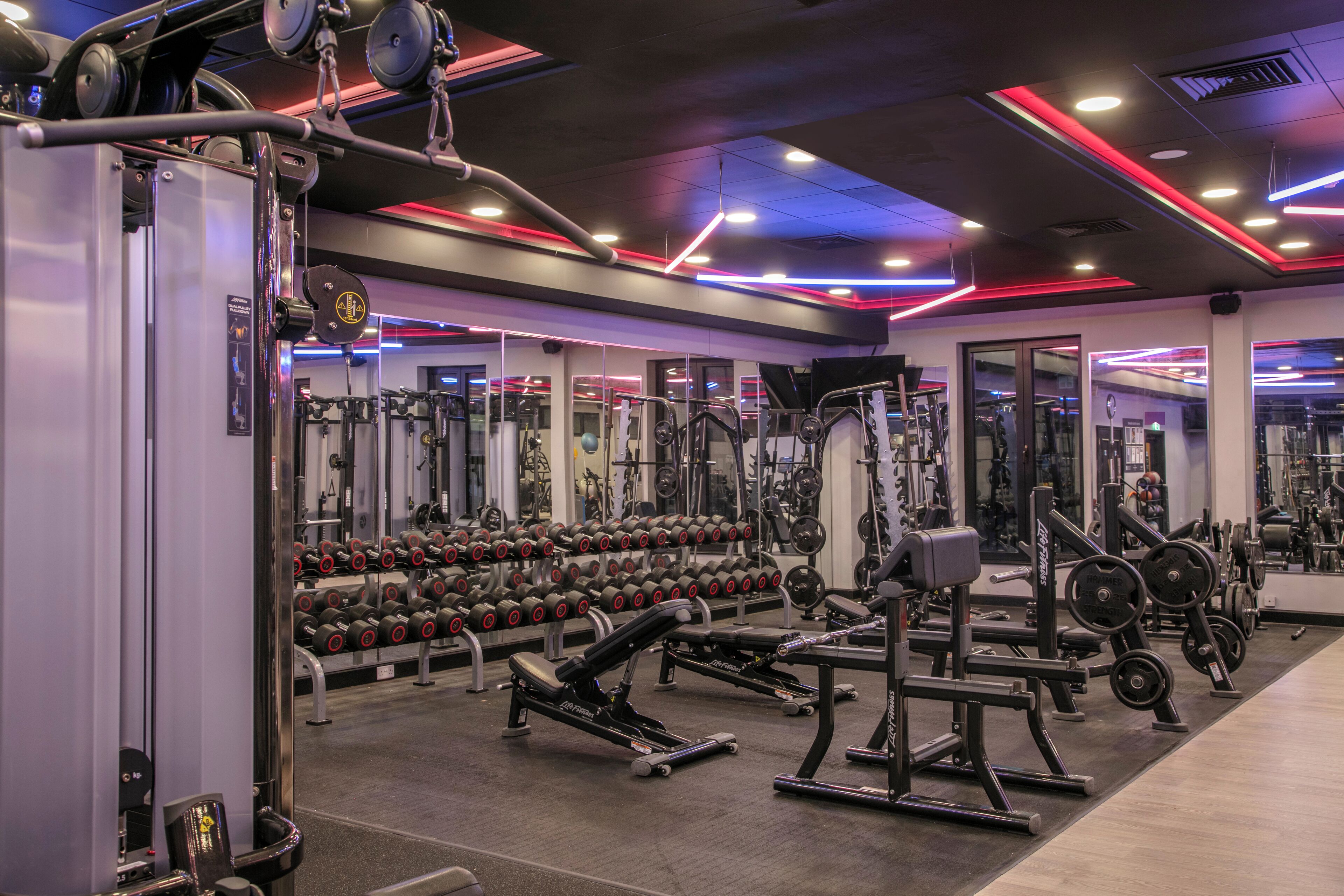 Un gimnasio con diverso equipo de ejercicio, estantes para pesas y espejos.