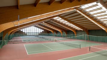Una cancha de tenis interior con un techo de madera alto y cortinas verdes.